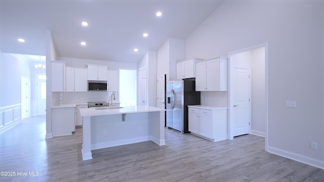 kitchen with light wood finished floors, light countertops, appliances with stainless steel finishes, and a kitchen island with sink