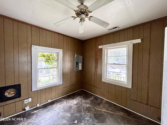 spare room featuring ceiling fan, wood walls, visible vents, and electric panel