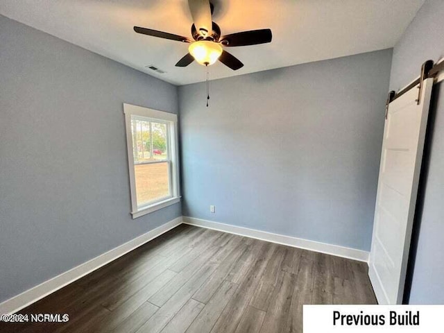 empty room featuring hardwood / wood-style floors, a barn door, and ceiling fan