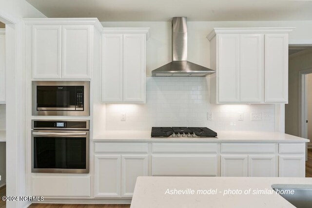 kitchen with wall chimney range hood, appliances with stainless steel finishes, tasteful backsplash, and wood-type flooring