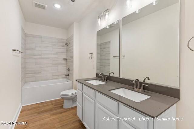 full bathroom with wood-type flooring, double sink vanity, toilet, and tiled shower / bath