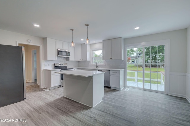 kitchen featuring white cabinetry, light hardwood / wood-style floors, decorative light fixtures, and appliances with stainless steel finishes