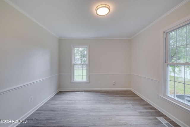 empty room featuring wood-type flooring, plenty of natural light, and ornamental molding