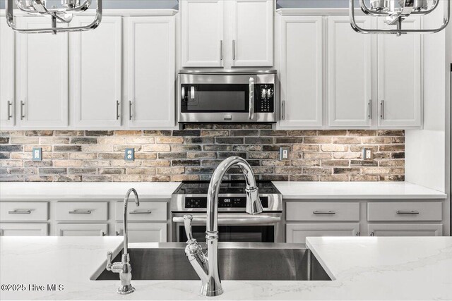 kitchen featuring white cabinetry, decorative light fixtures, light wood-type flooring, appliances with stainless steel finishes, and light stone countertops