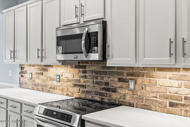 kitchen with stainless steel refrigerator with ice dispenser, white cabinetry, and brick wall