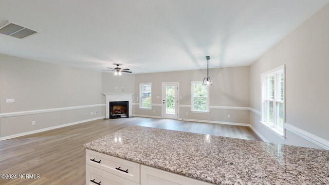 kitchen with decorative light fixtures, white cabinets, ceiling fan, light stone countertops, and light hardwood / wood-style flooring