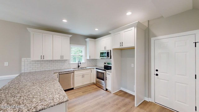 kitchen with appliances with stainless steel finishes, sink, white cabinets, backsplash, and light stone counters