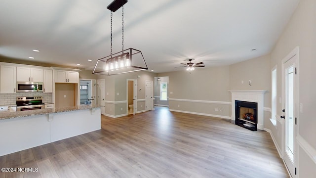 kitchen with white cabinetry, light stone counters, decorative light fixtures, stainless steel appliances, and decorative backsplash