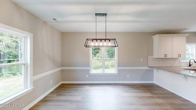 kitchen with light stone counters, tasteful backsplash, light hardwood / wood-style flooring, hanging light fixtures, and white cabinets