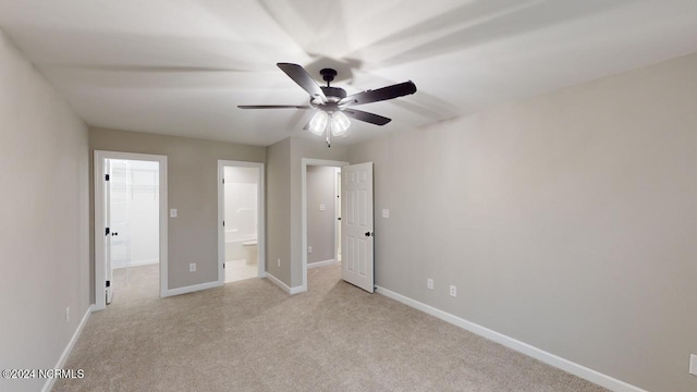 unfurnished bedroom with ensuite bath, a walk in closet, light carpet, a closet, and ceiling fan