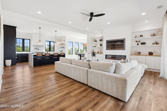 living room with ceiling fan, plenty of natural light, light hardwood / wood-style floors, and built in features