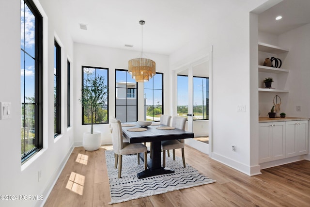 dining room featuring an inviting chandelier, built in shelves, and light hardwood / wood-style floors