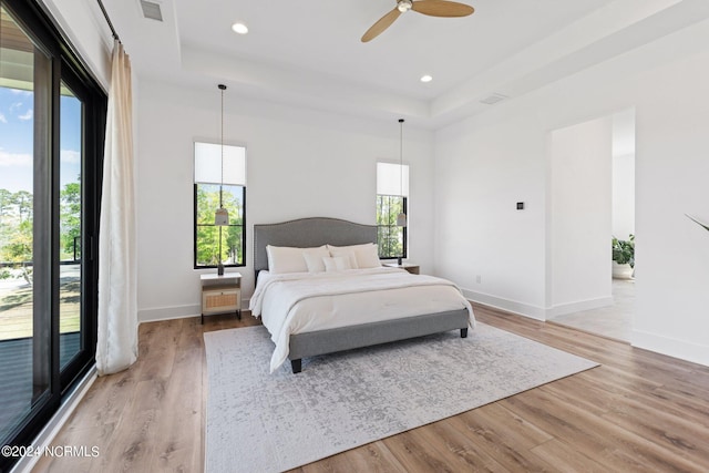 bedroom with a raised ceiling, access to exterior, ceiling fan, and light hardwood / wood-style flooring