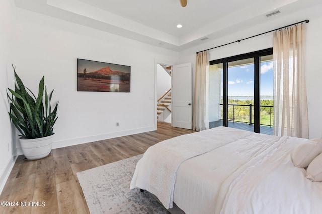 bedroom with a raised ceiling, wood-type flooring, and access to outside