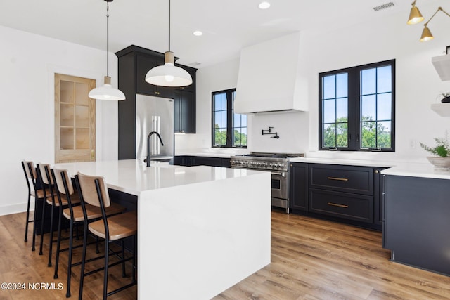 kitchen with premium range hood, appliances with stainless steel finishes, pendant lighting, a kitchen bar, and a center island with sink