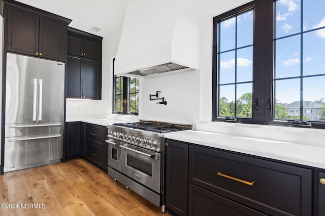 kitchen featuring light hardwood / wood-style floors, stainless steel appliances, custom range hood, and a healthy amount of sunlight