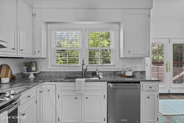 kitchen with appliances with stainless steel finishes, white cabinetry, sink, backsplash, and dark stone counters