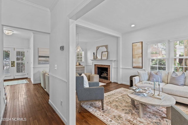 living room with a brick fireplace, crown molding, dark wood-type flooring, and french doors