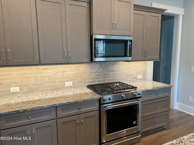 kitchen featuring backsplash, gray cabinets, light stone counters, appliances with stainless steel finishes, and dark hardwood / wood-style flooring