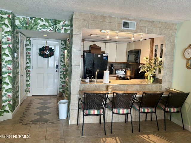 kitchen with visible vents, a breakfast bar, a textured ceiling, black appliances, and a sink