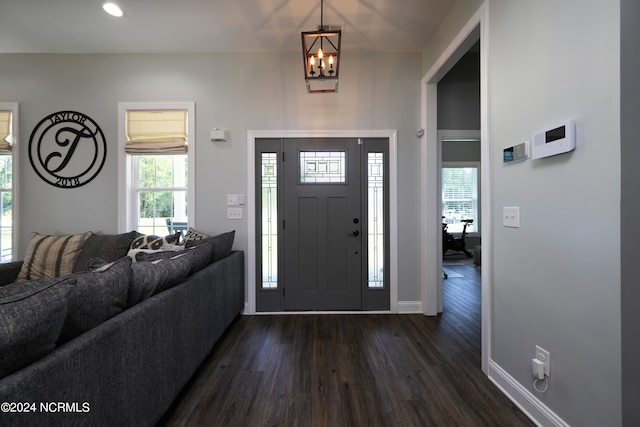 foyer entrance with dark wood-type flooring, plenty of natural light, and an inviting chandelier