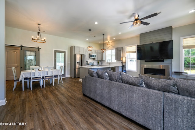 living room featuring a barn door, dark wood-type flooring, sink, and ceiling fan with notable chandelier