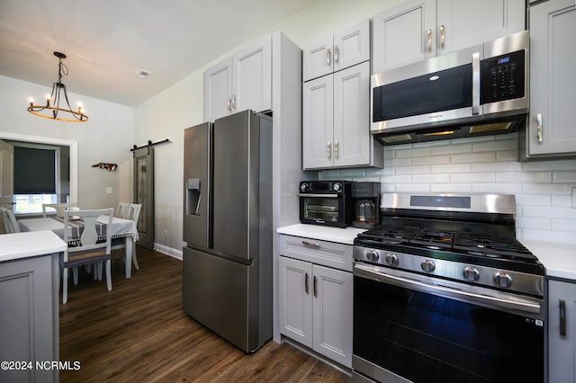 kitchen with a barn door, backsplash, a notable chandelier, stainless steel appliances, and dark hardwood / wood-style flooring