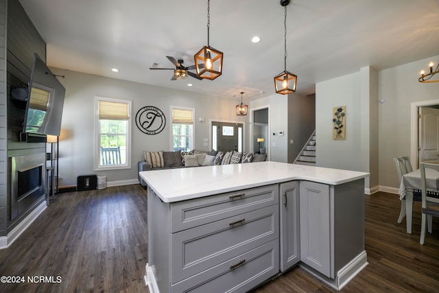 kitchen featuring ceiling fan, dark hardwood / wood-style floors, gray cabinets, pendant lighting, and a large fireplace