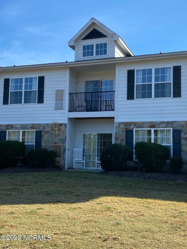 exterior space featuring stone siding, a lawn, and a balcony