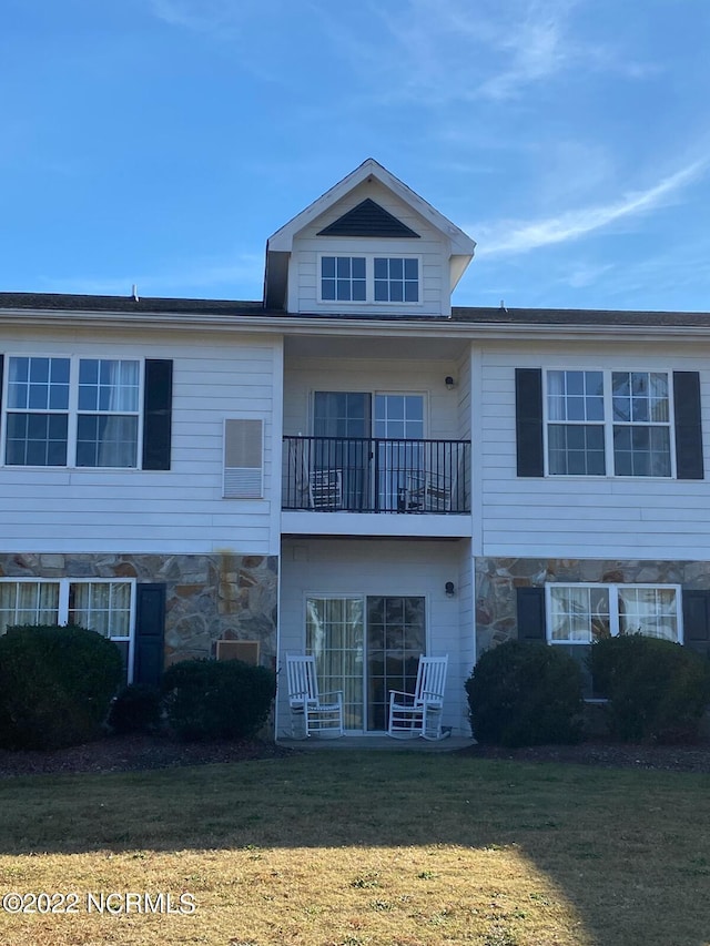 view of front of home with stone siding, a balcony, and a front lawn