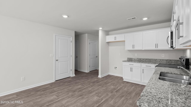 kitchen with white cabinetry, sink, light stone counters, and light hardwood / wood-style flooring