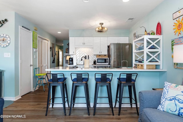 kitchen featuring tasteful backsplash, dark hardwood / wood-style flooring, white cabinets, stainless steel refrigerator, and kitchen peninsula