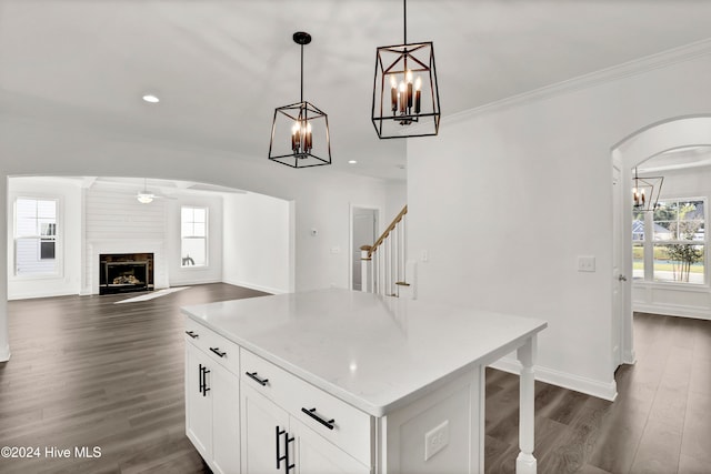 kitchen featuring dark wood-type flooring, crown molding, decorative light fixtures, white cabinets, and a kitchen island