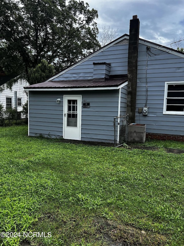 back of property featuring metal roof, a yard, and a chimney