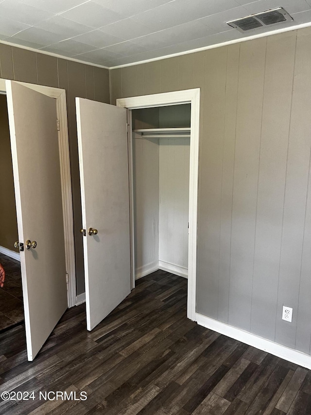 unfurnished bedroom with dark wood-style floors, a closet, and visible vents