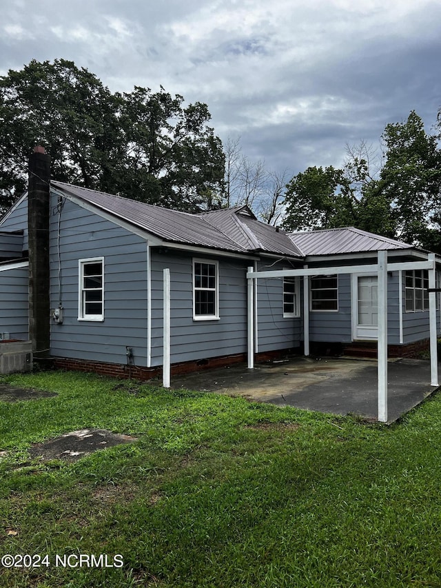 rear view of house with metal roof, a lawn, and a patio area