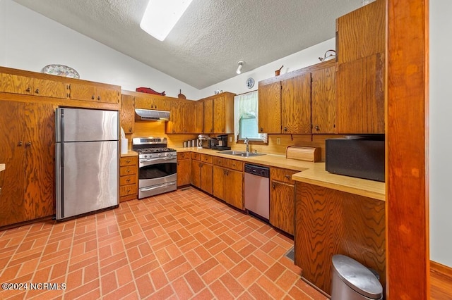 kitchen with under cabinet range hood, a sink, light countertops, appliances with stainless steel finishes, and brown cabinetry