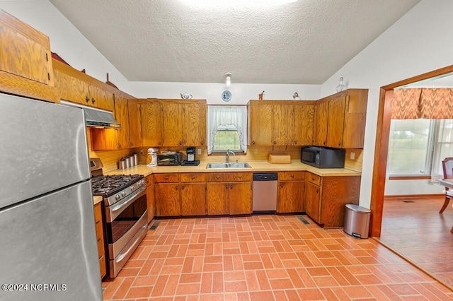 kitchen with brown cabinets, range hood, stainless steel appliances, light countertops, and a sink