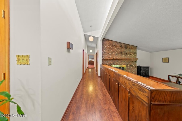 corridor with vaulted ceiling with beams, a textured ceiling, baseboards, and wood finished floors