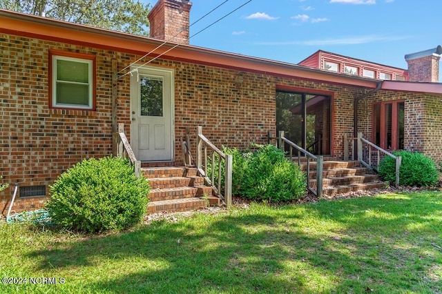 property entrance featuring crawl space, brick siding, a lawn, and a chimney