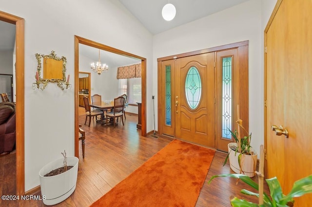 entryway with lofted ceiling, baseboards, wood finished floors, and an inviting chandelier