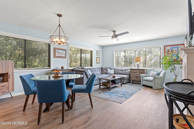 dining space with ceiling fan with notable chandelier, a fireplace, and light wood-style flooring