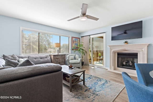 living area with a ceiling fan, a fireplace with raised hearth, and light wood finished floors