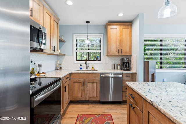 kitchen featuring hanging light fixtures, appliances with stainless steel finishes, light stone counters, and a sink