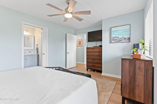 bedroom featuring a ceiling fan, ensuite bath, light wood-style flooring, and baseboards