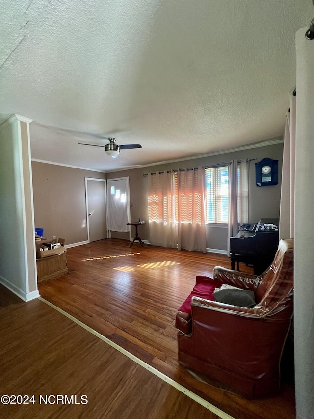 living room featuring crown molding, ceiling fan, wood-type flooring, and a textured ceiling