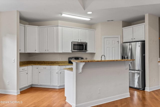 kitchen featuring a kitchen island with sink, appliances with stainless steel finishes, light wood-type flooring, and white cabinets