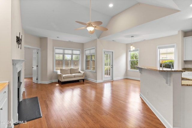 unfurnished living room with sink, ceiling fan, vaulted ceiling, and light wood-type flooring