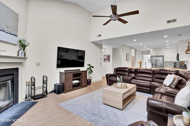 living room with ceiling fan, light hardwood / wood-style flooring, sink, and high vaulted ceiling