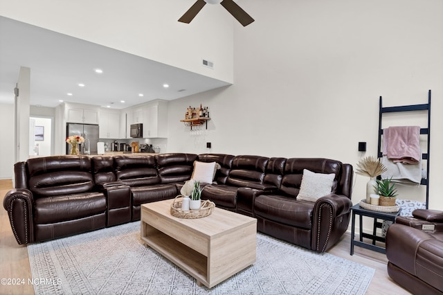 living room featuring ceiling fan, light hardwood / wood-style flooring, and a high ceiling